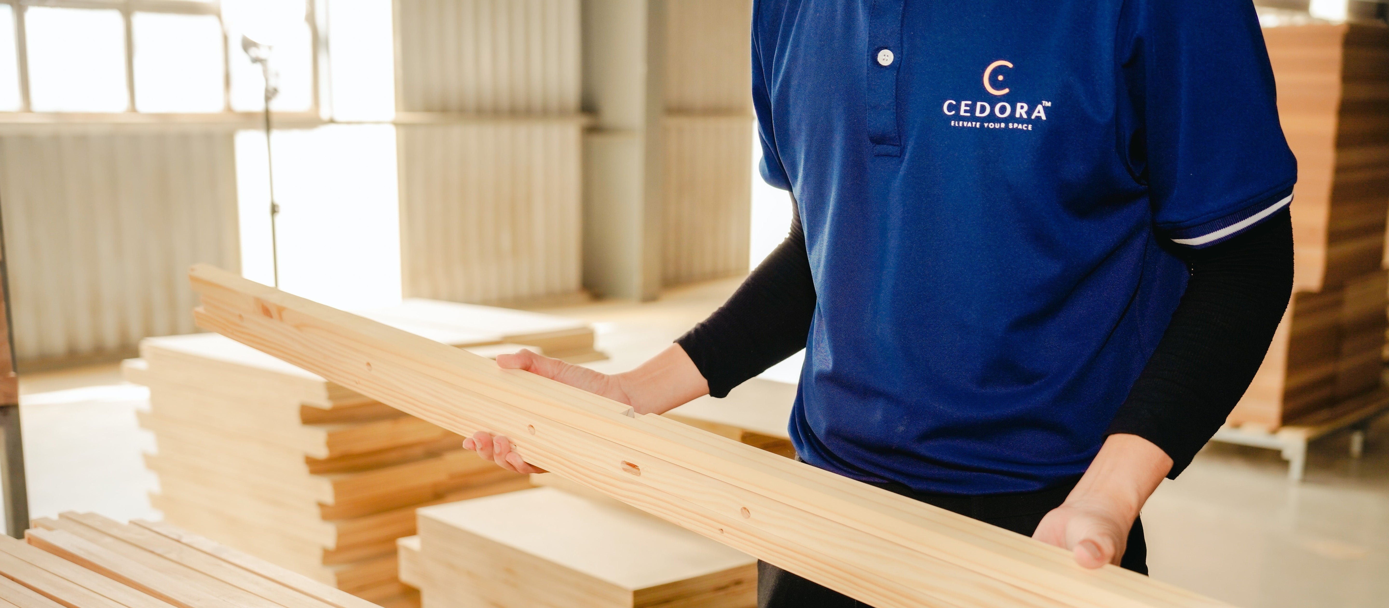 Person holding a wooden plank in a workshop with 'CEDORA' branding.
