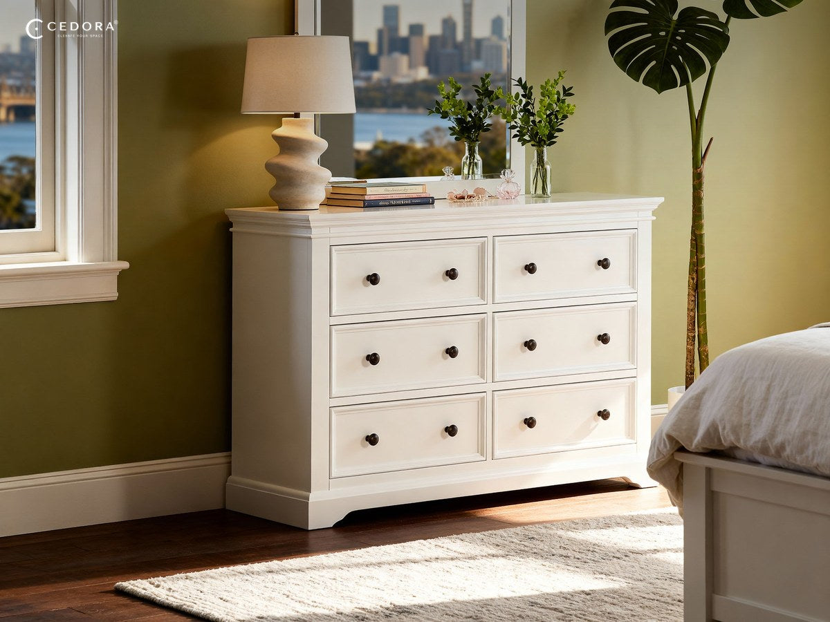 London mirror in white standing on a six drawer chest, reflecting a city skyline through a bedroom window