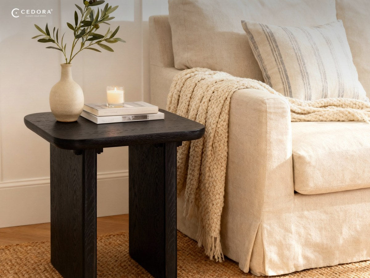 Black timber side table with a vase and books beside a cream sofa on a jute rug