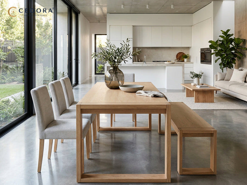 Richmond dining table in pale timber with a matching bench along one side and upholstered chairs, in an open plan room with concrete floors