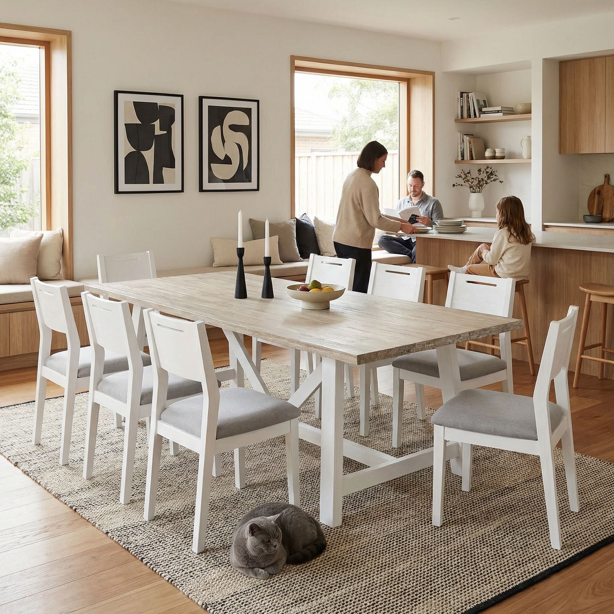 Modern dining room with a wooden table and chairs, people in the background, and a cat on the floor.

