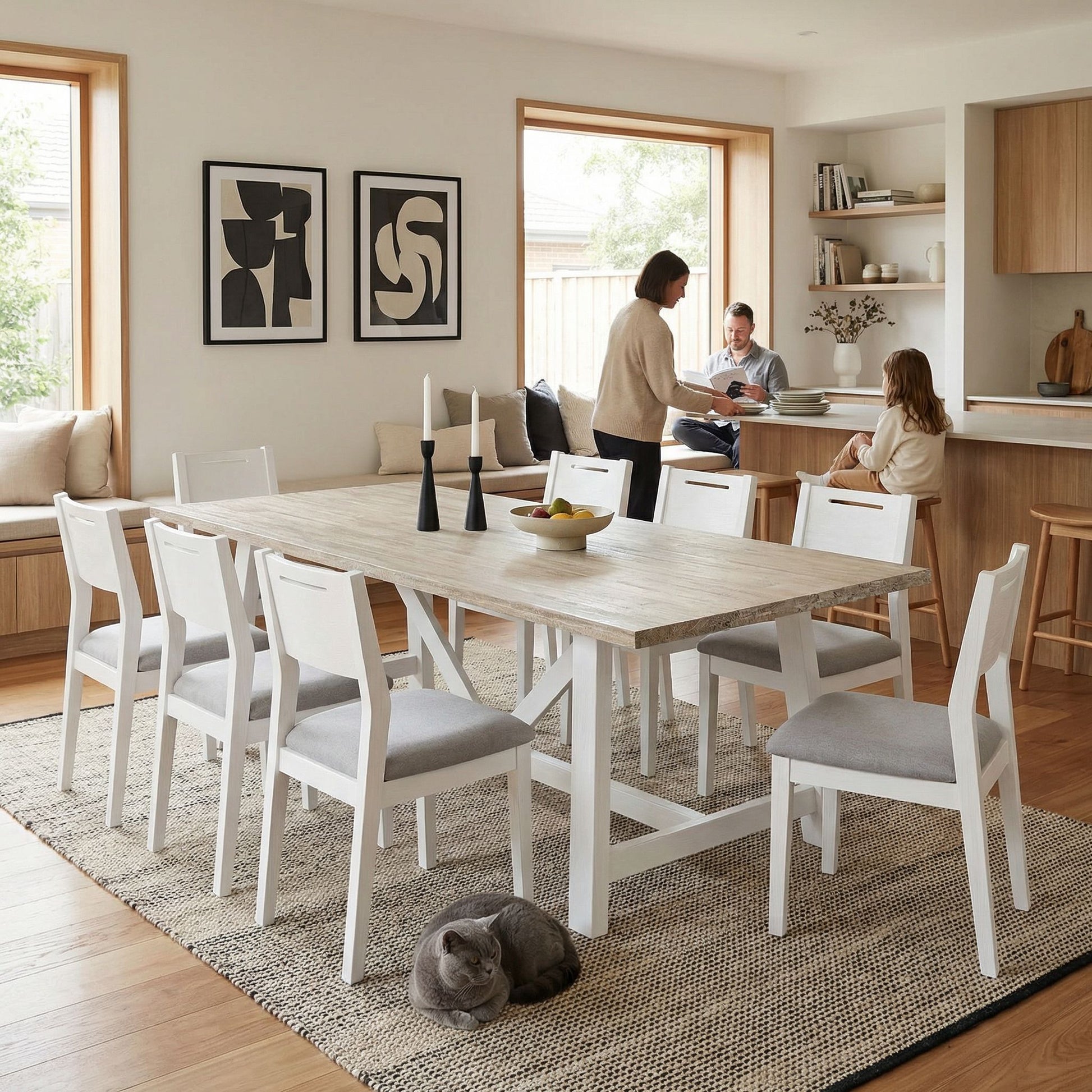 Modern dining room with a wooden table and chairs, people in the background, and a cat on the floor.

