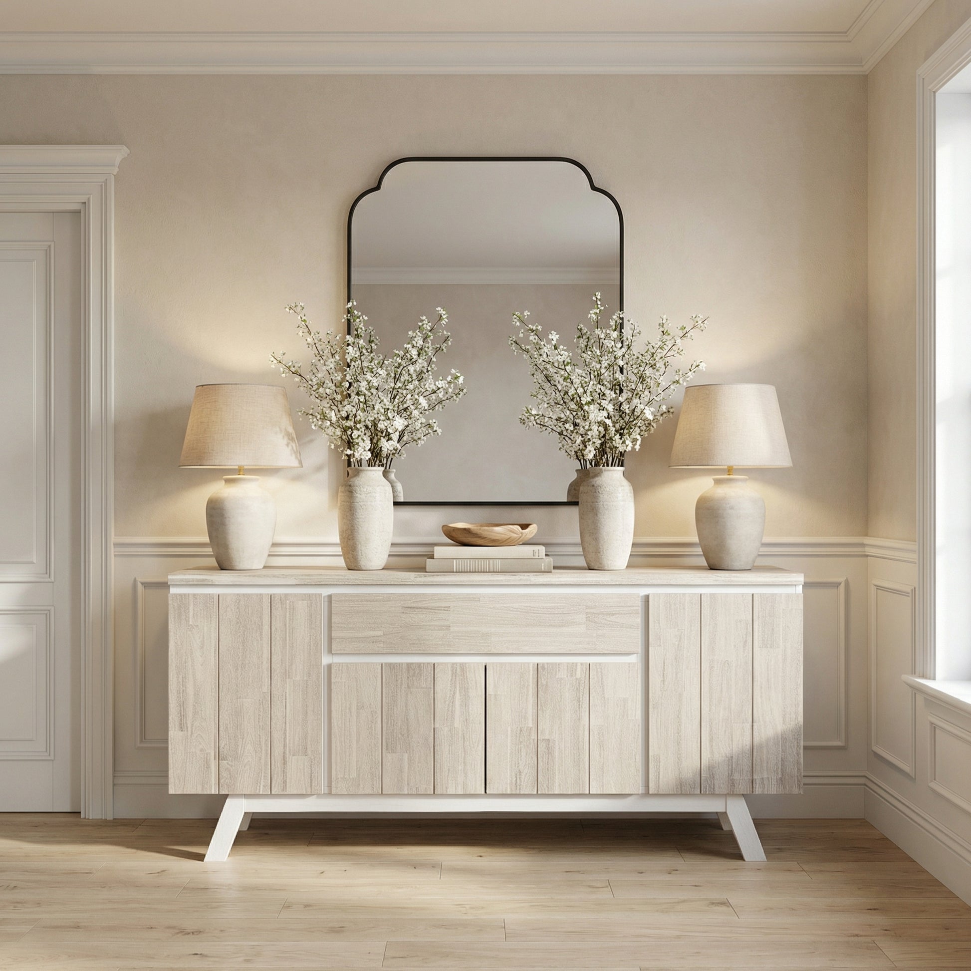 Light wood sideboard with two lamps, two vases with white flowers, and a mirror in a room.

