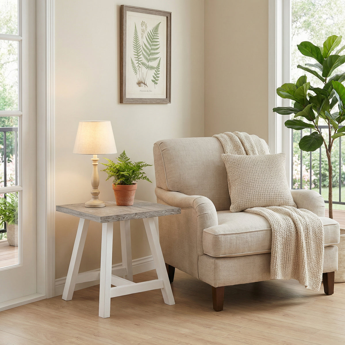 Beige armchair with a blanket and pillow in a living room setting with a side table, lamp, and plants.

