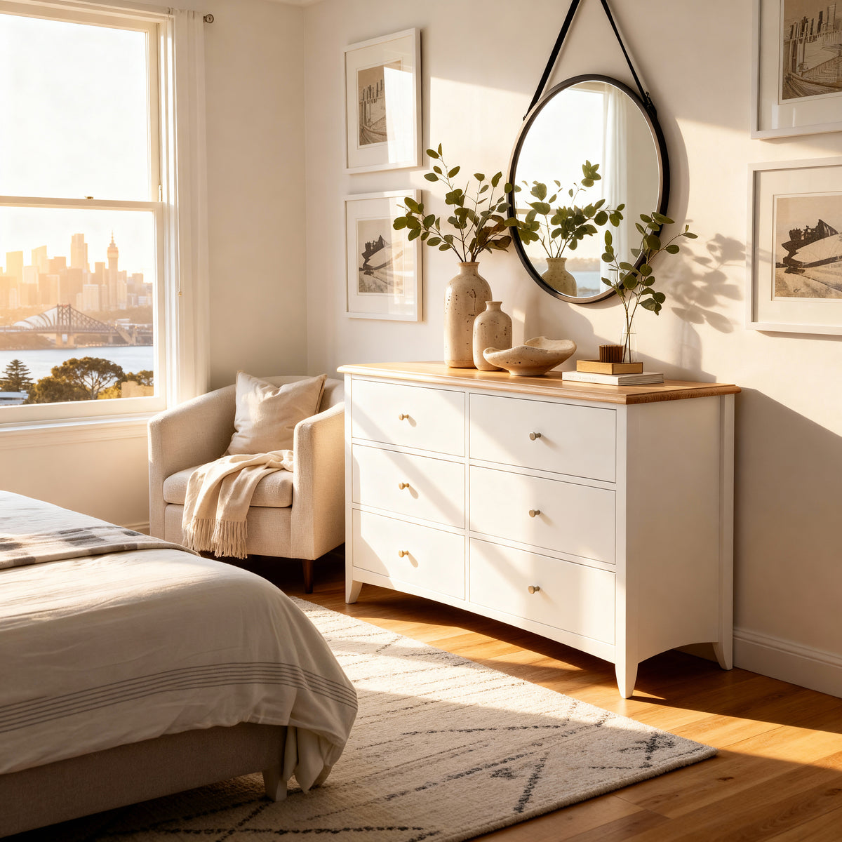 Bristol Pine 6 Drawer Chest below a round black framed mirror with trailing greenery, beside an armchair in golden light