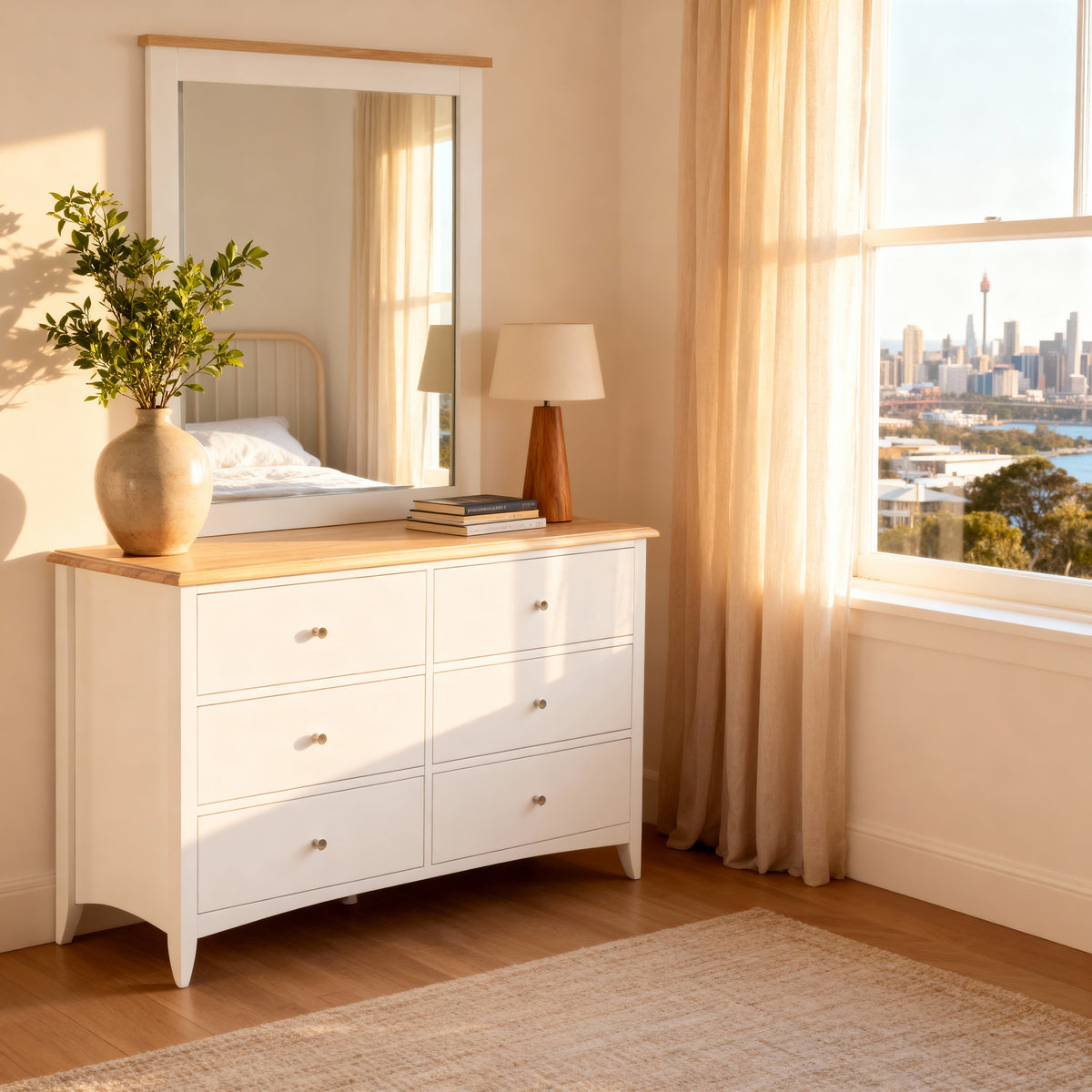 Bristol Pine Mirror hung above a matching chest holding olive stems and a lamp, by a city skyline window