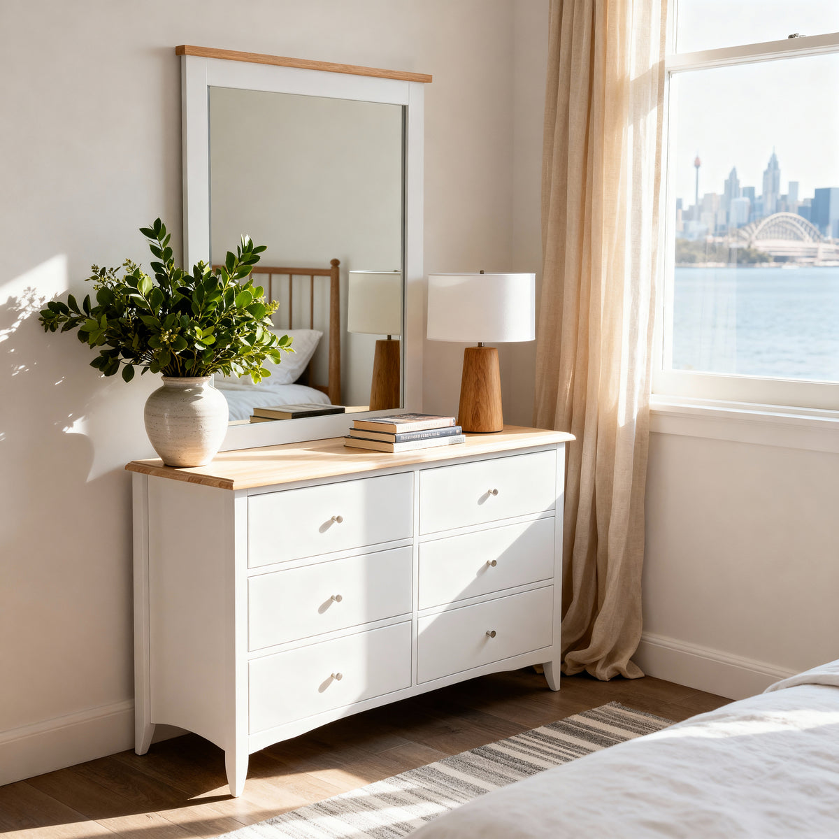 Bristol Pine 6 Drawer Chest with Mirror topped with greenery and a lamp below a matching mirror, by a harbour window
