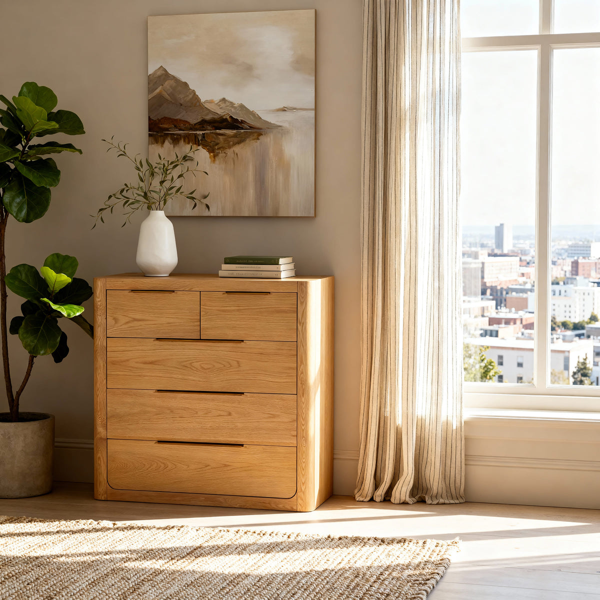 Liverpool Pine 5 Drawer Tallboy - Natural below a mountain landscape painting, beside a fiddle leaf fig by a city window