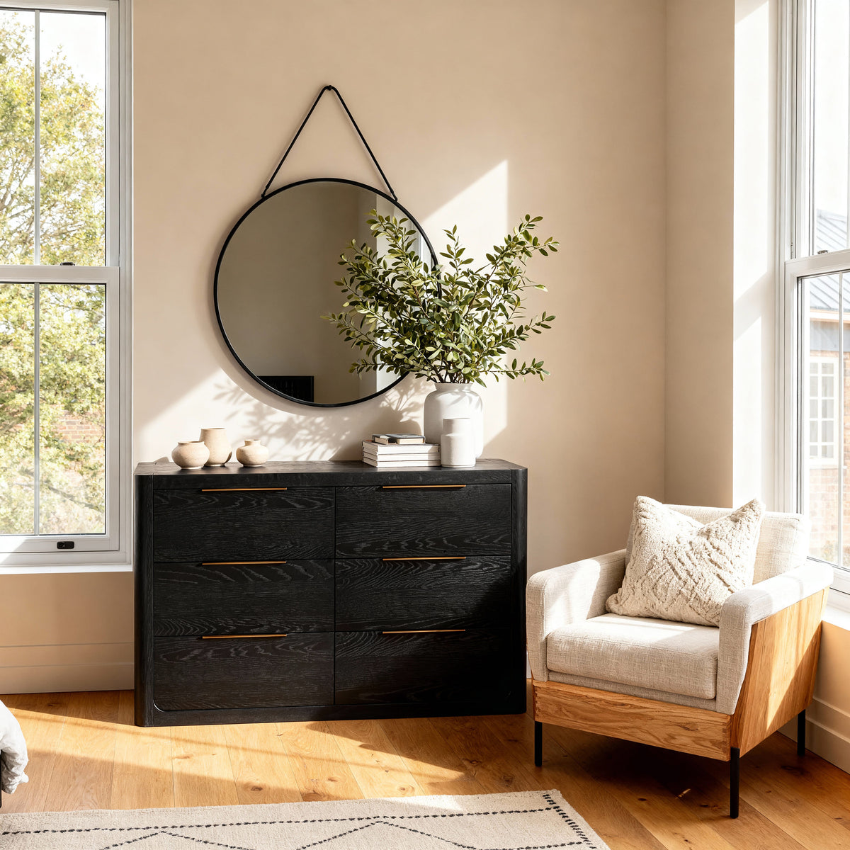 Liverpool Pine 6 Drawer Chest - Black below a round mirror on a leather strap, topped with greenery beside a tan armchair