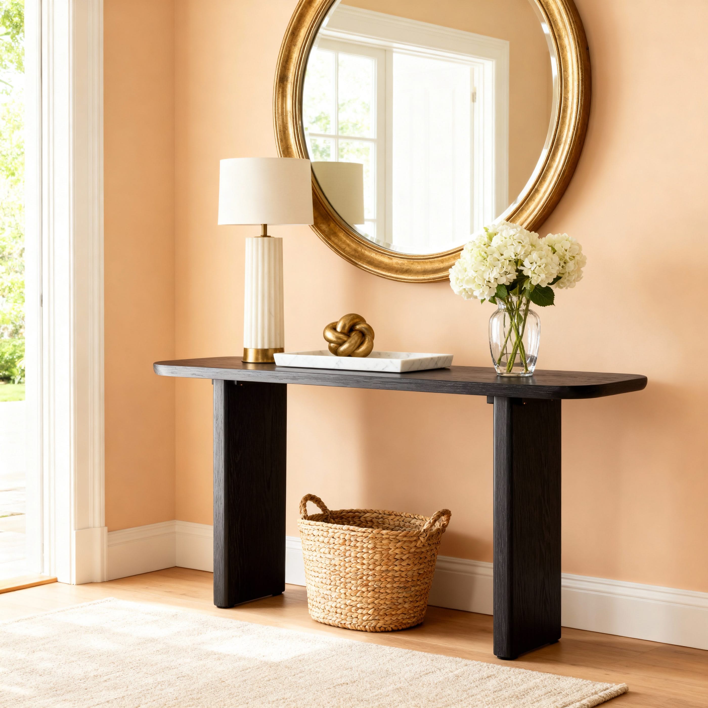 Console table with lamp, decorative items, and flowers against a peach wall.


