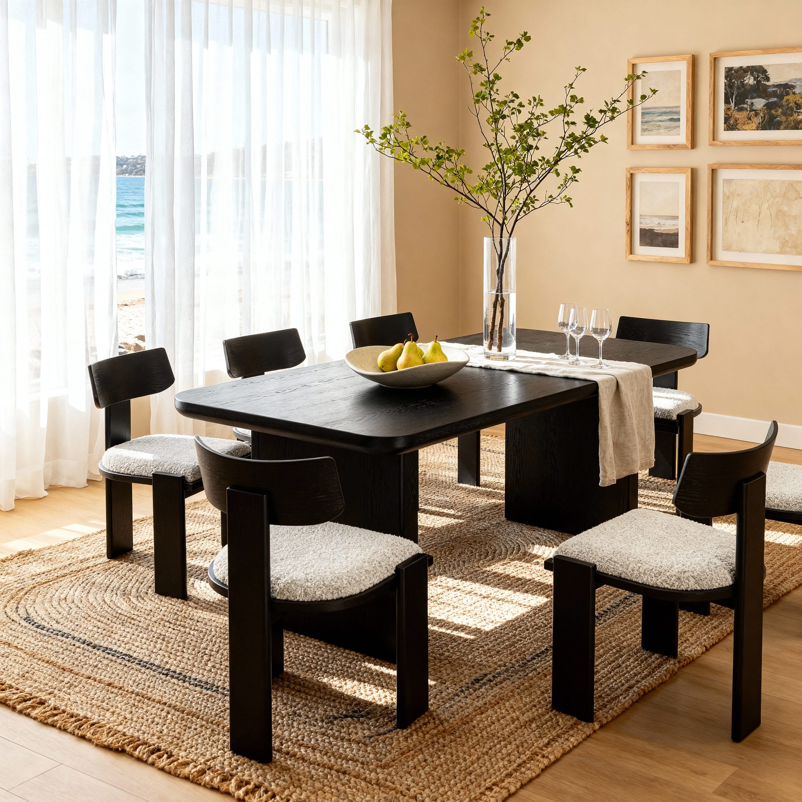 Dining room with black table and chairs on a jute rug, featuring a bowl of fruit and a vase.

