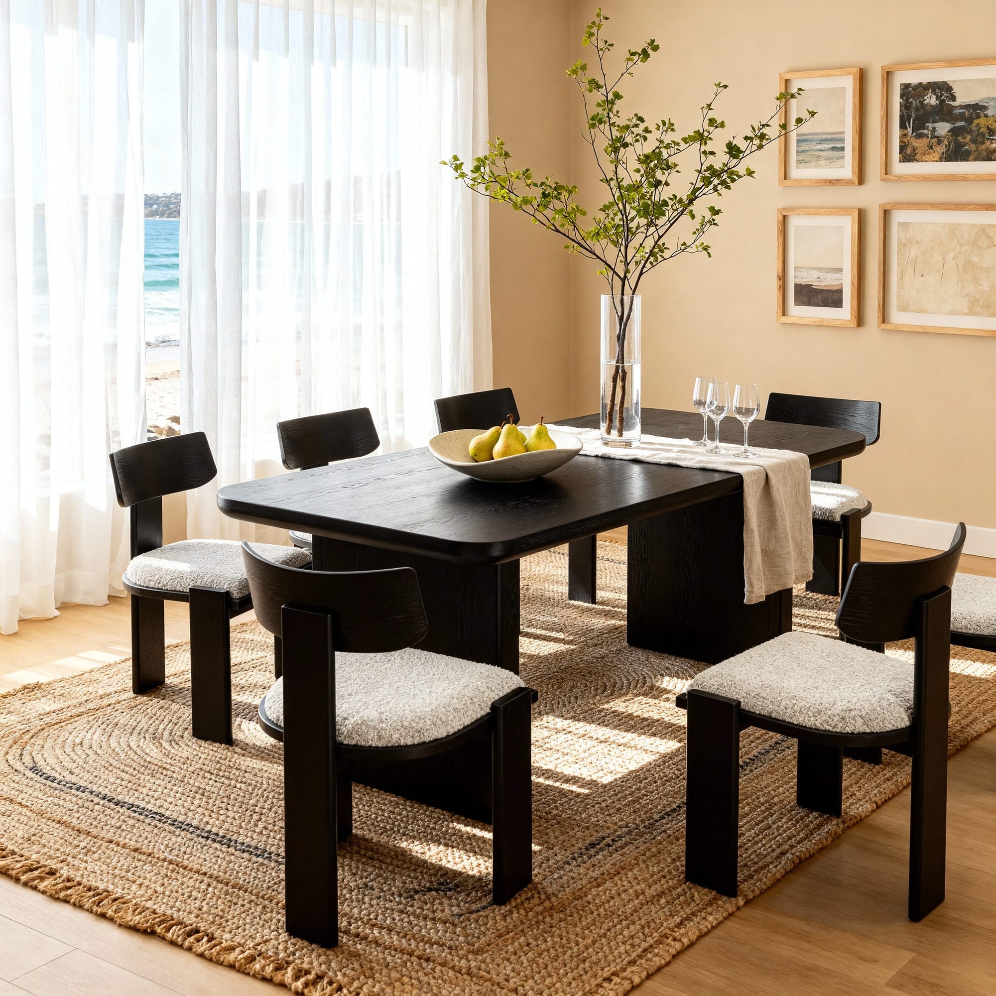 Dining room with black table and chairs on a jute rug, featuring a bowl of fruit and a vase.

