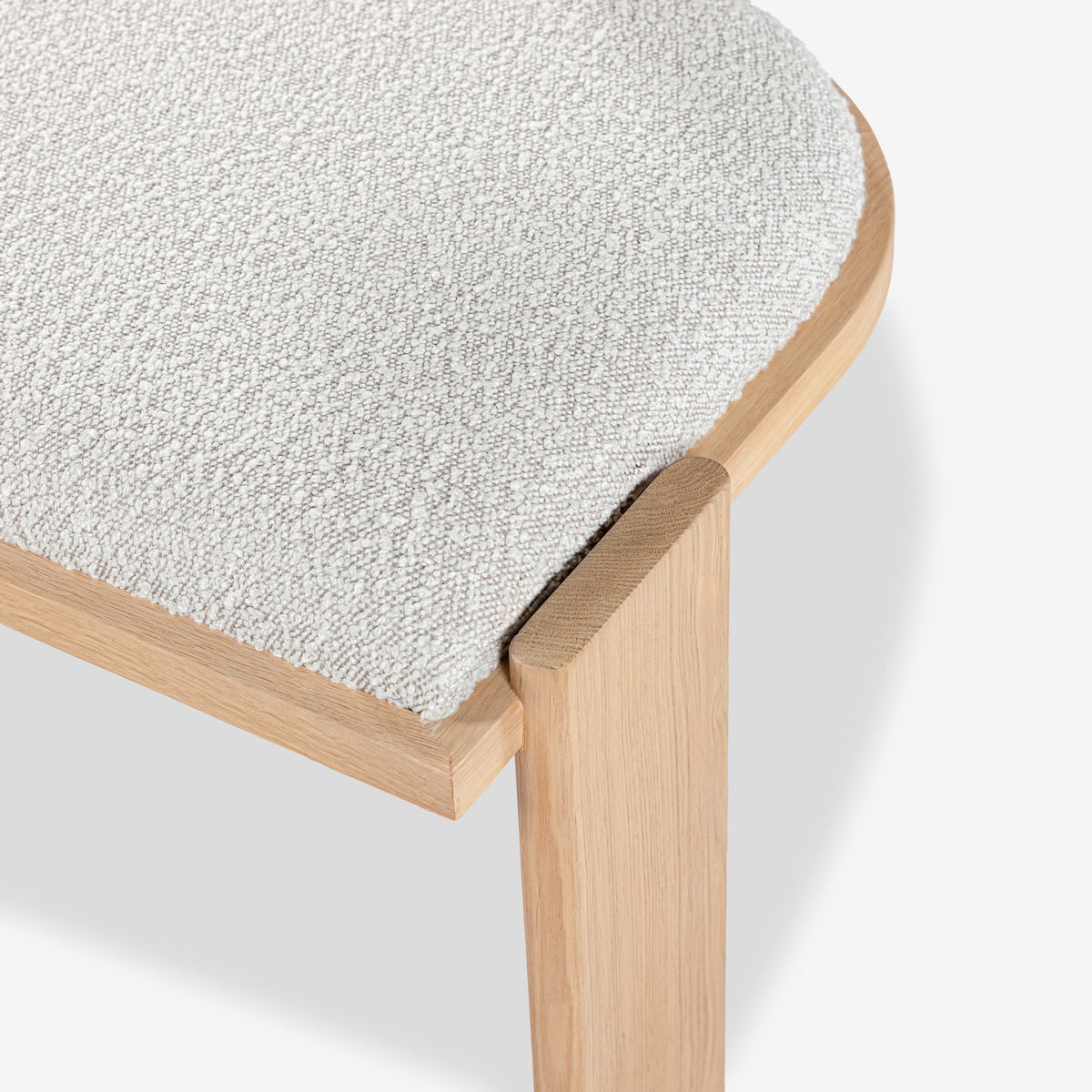 Close-up of a stool with a textured white seat and wooden frame on a light background

