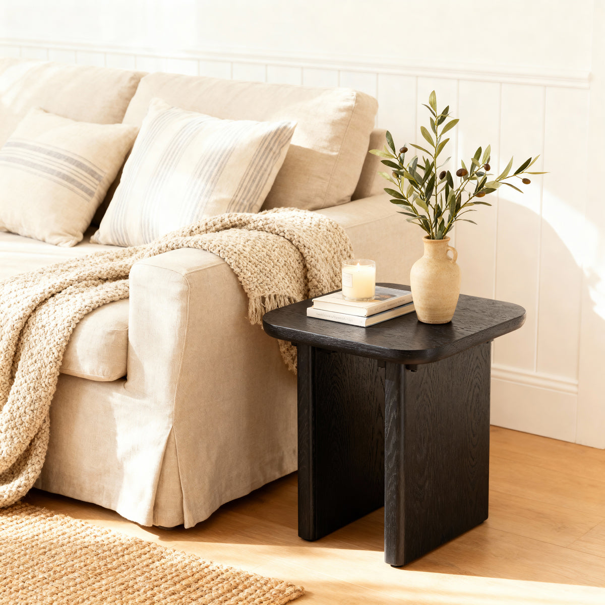 Black side table with a vase and candle next to a beige sofa in a living room.

