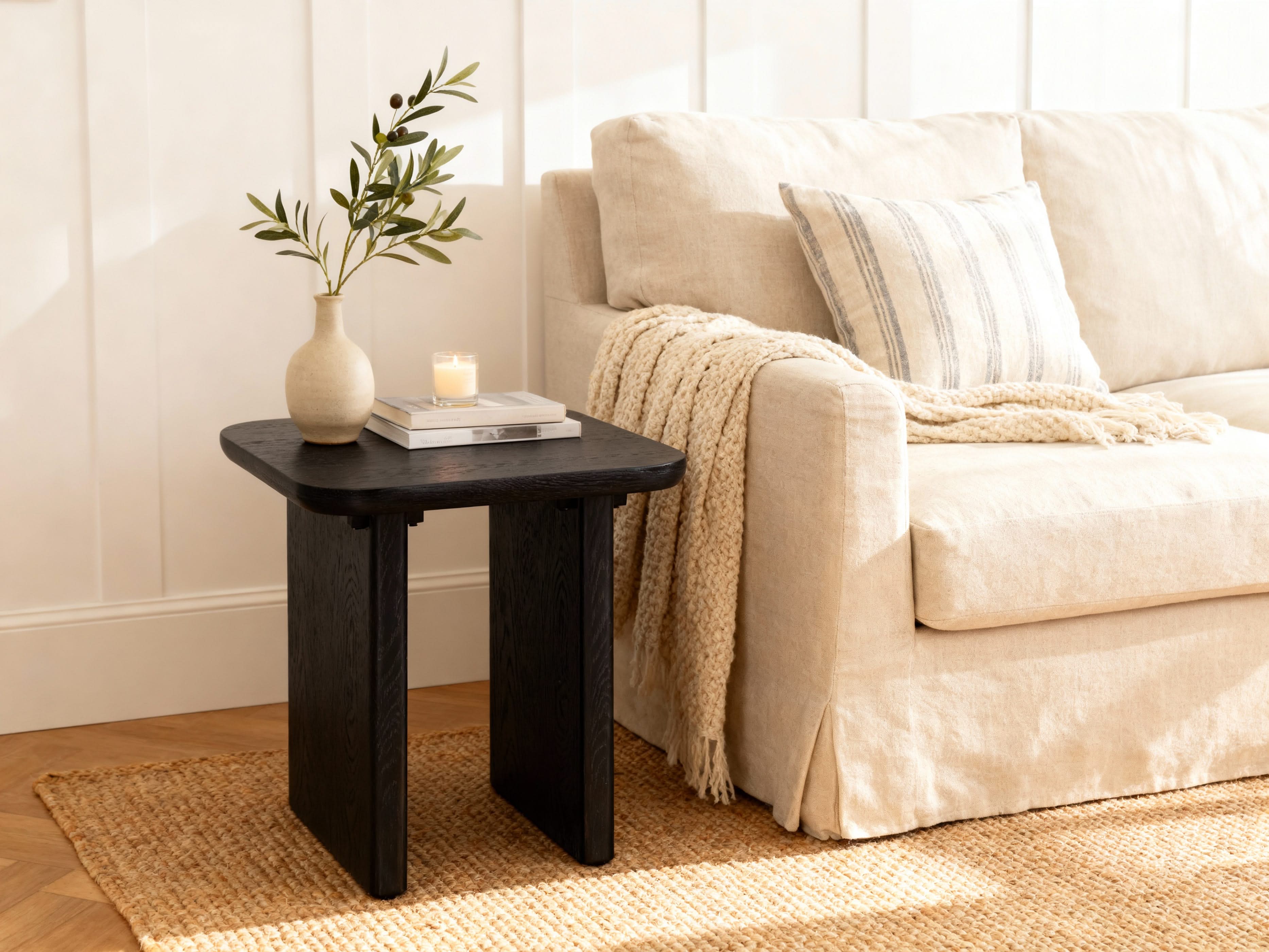 Black side table with a plant and candle next to a beige sofa in a living room.

