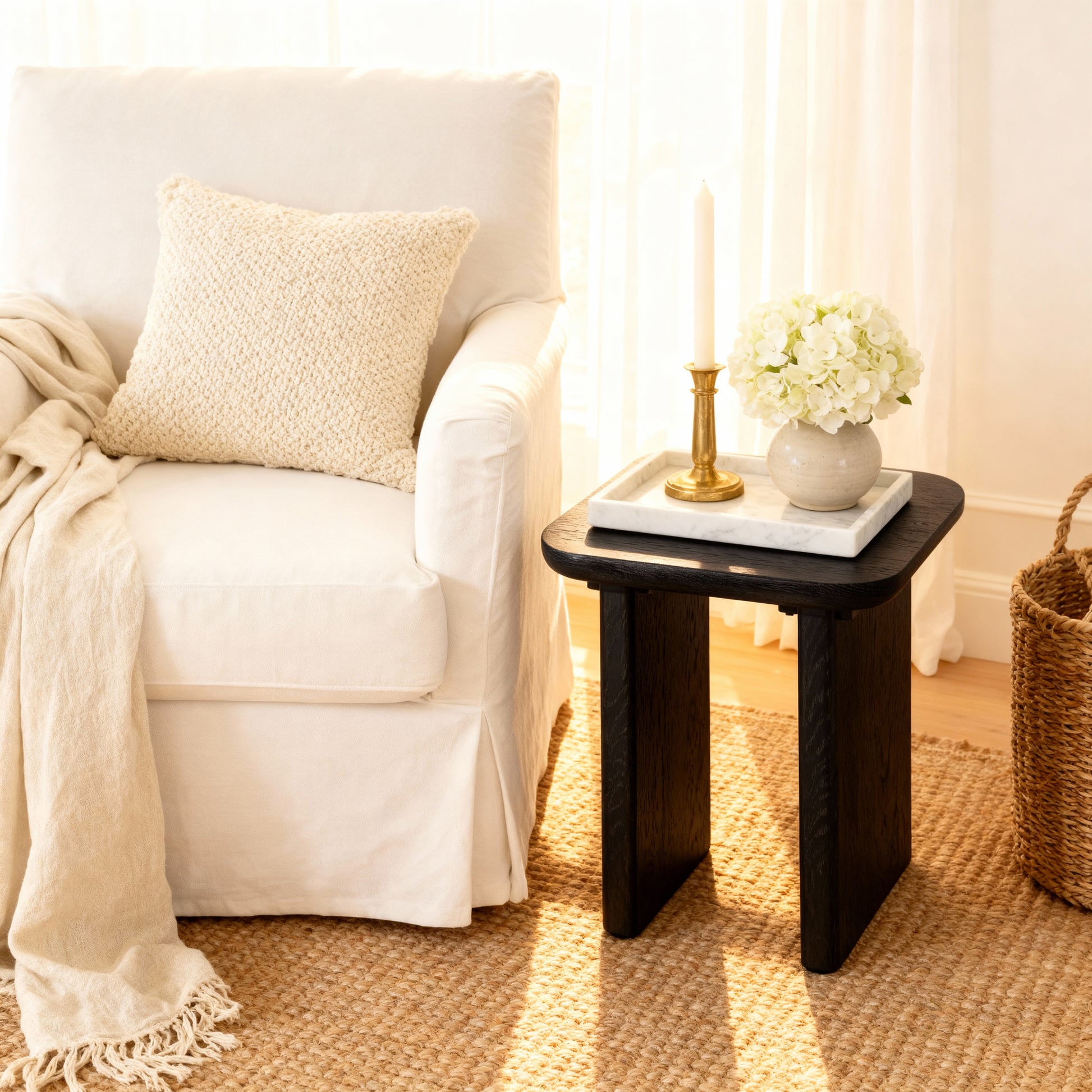 Black side table with decorative items next to a white armchair in a cozy living room.

