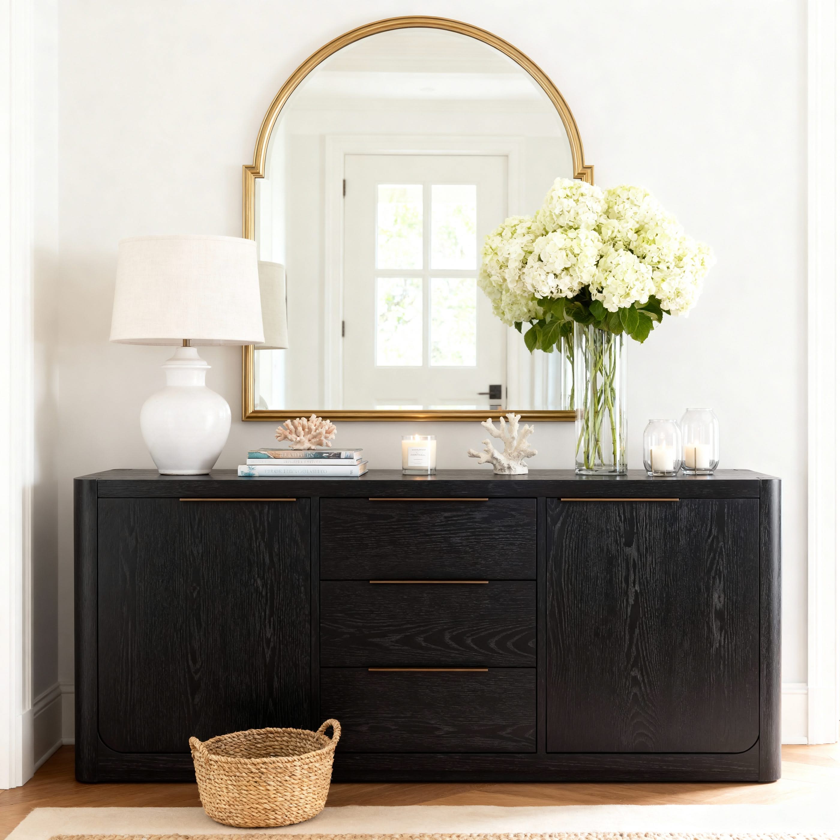 Black dresser with gold-framed mirror, white flowers, and decor items in a room.

