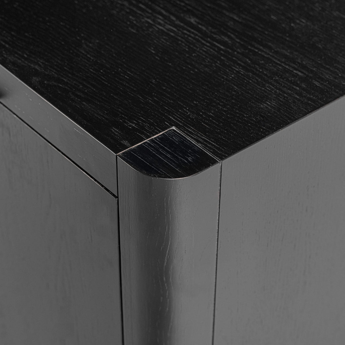Close-up of a corner where a dark wood surface meets a light gray wall.

