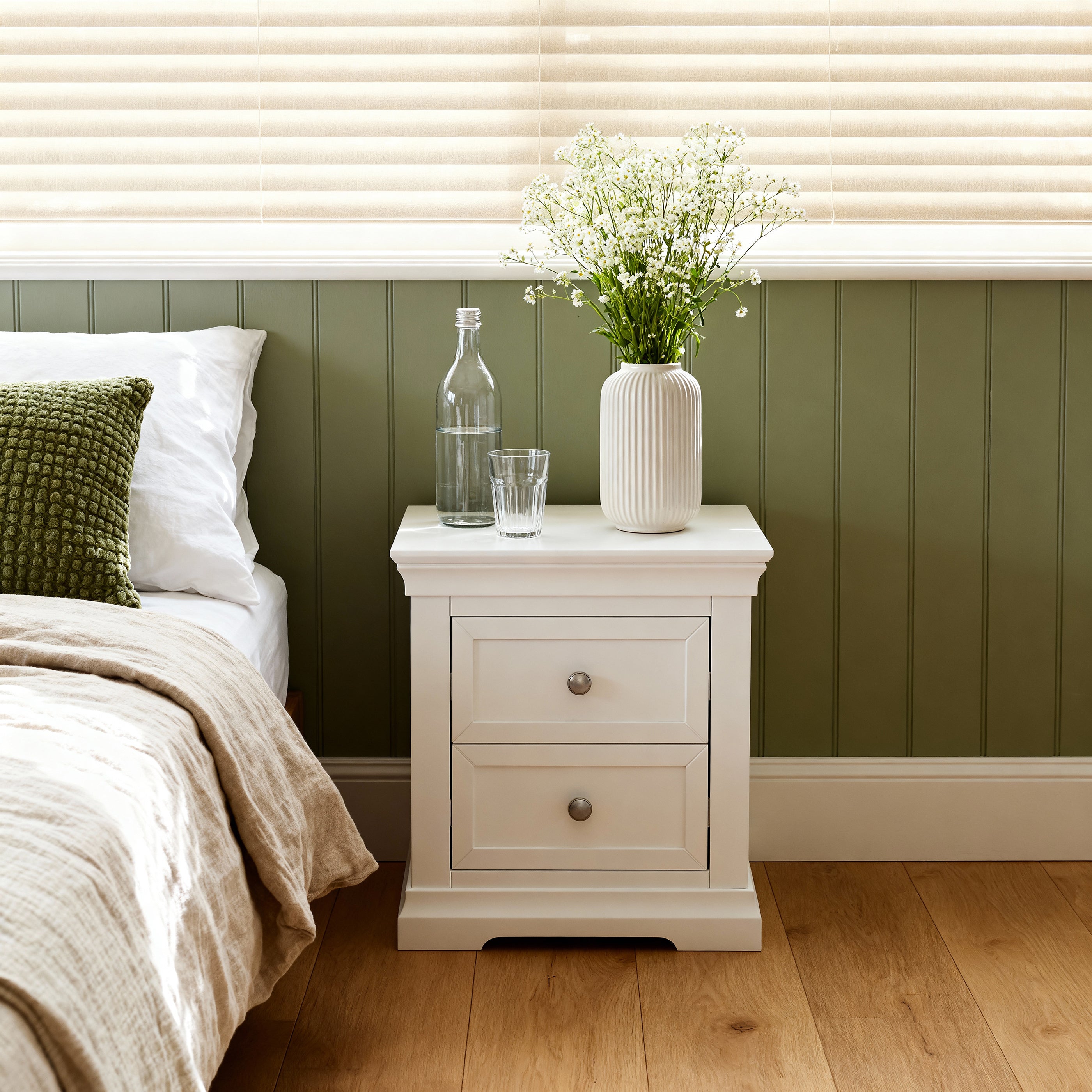 White nightstand with decorative items next to a bed with green and white bedding.


