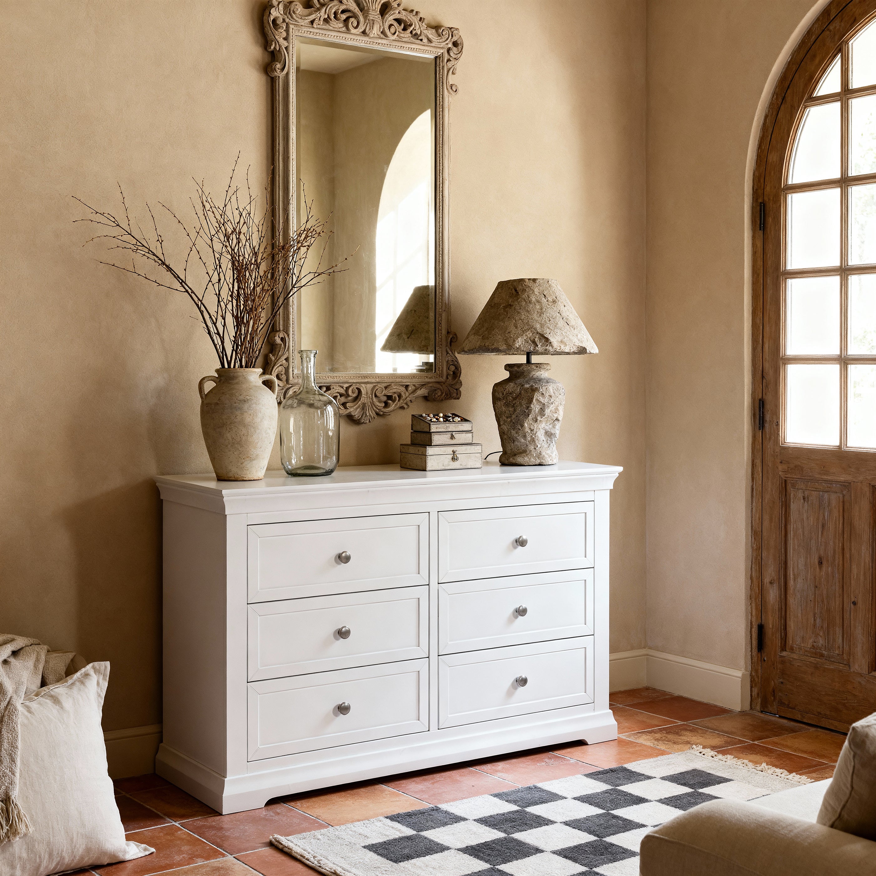 White dresser with decorative items in a room with a mirror and lamp.


