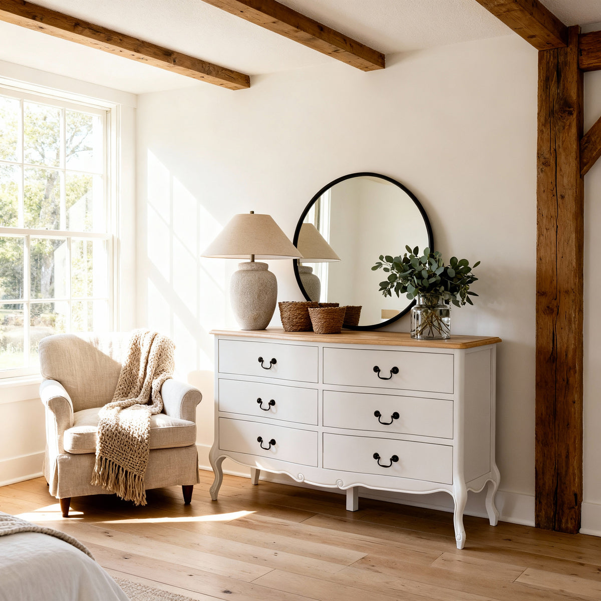 Newcastle Acacia 6 Drawer Chest below a round black mirror under exposed beams, topped with a lamp and olive stems