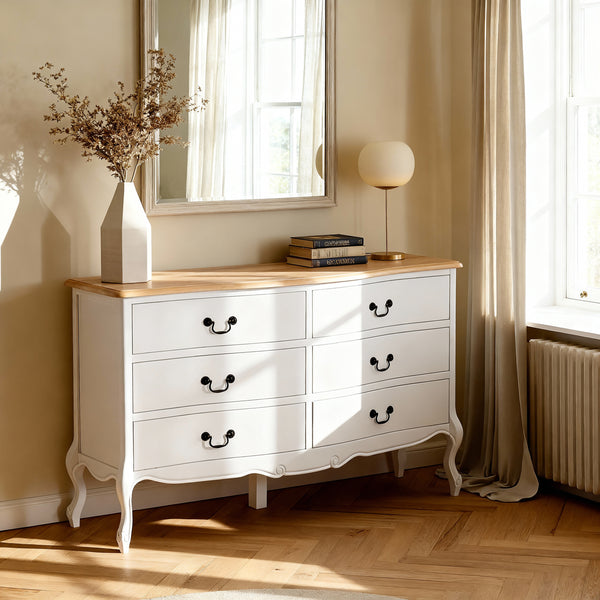 Newcastle Acacia 6 Drawer Chest below a rectangular mirror, topped with dried stems and a globe lamp on parquet floors