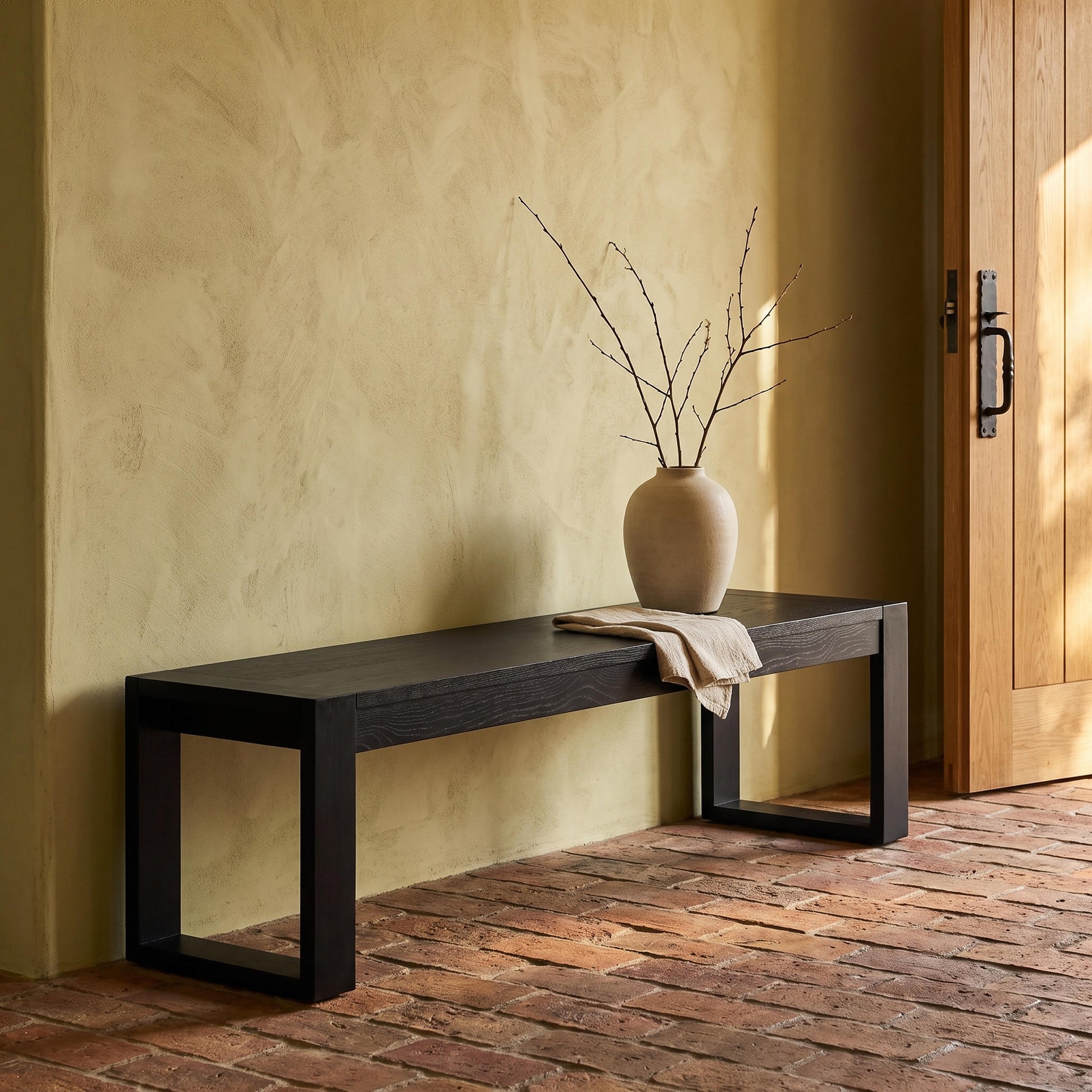 Richmond Pine Dining Bench 200cm - Black against an ochre wall, draped with a throw beside a stoneware vase of stems